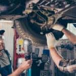 two car mechanics under a lifted car fixing the brakes