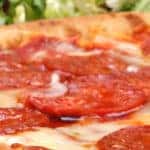 Fresh-baked pepperoni pizza with a partial view of a salad in the background.