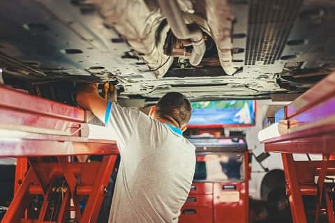 mechanic working on the underside of a car at a dealership