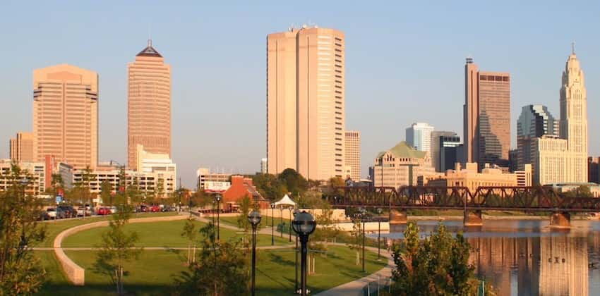 A park against a river with the Columbus skyline against a blue sky