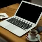 A laptop, coffee, phone and notebook on a table