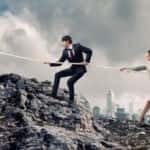 People in suits holding a rope climbing rocks