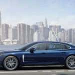 A blue Porsche Panamera 4s on a highway in front of the New York City skyline