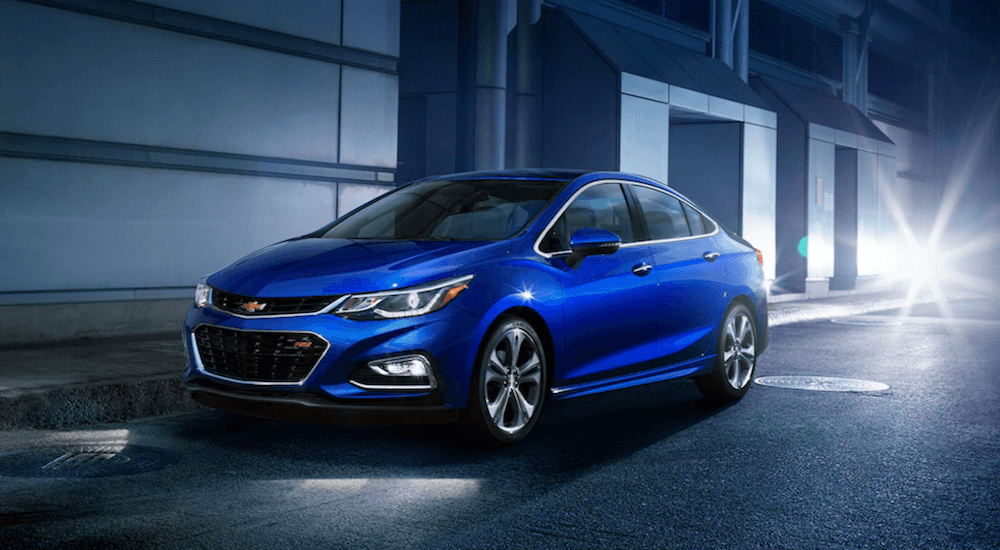 Front angled view of a blue Chevy Cruze for sale parked by an industrial building