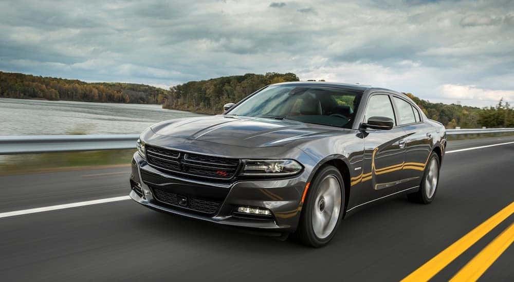 A dark gray used Dodge Charger drives down a coastal highway on a cloudy day.