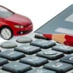Closeup of calculator with red pencil and red toy car in background, on white