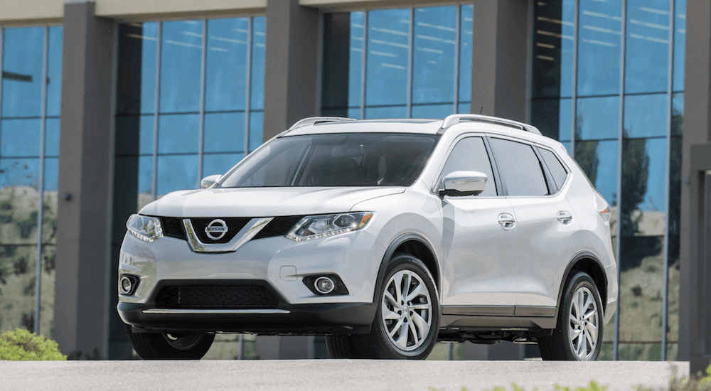 Front view of a white Nissan Rogue parked in front of a glass building