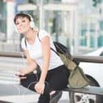 A college student is sitting at a bus stop listening to music. To get a car she will look into no credit car loans in Columbus.