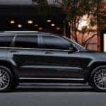 A black 2018 Jeep Grand Cherokee is parking outside a building a night. The Grand Cherokee is popular among used Jeeps for sale in Indianapolis.