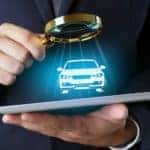 A close up of a man holding a tablet and a magnifying glass with a virtual car is searching for an alternative to Buy Here Pay Here in Columbus Ohio.