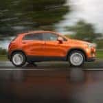 An orange 2016 Chevy Trax, a popular model for used Chevy SUVs for sale in Indianapolis, IN, is driving on a wet road.