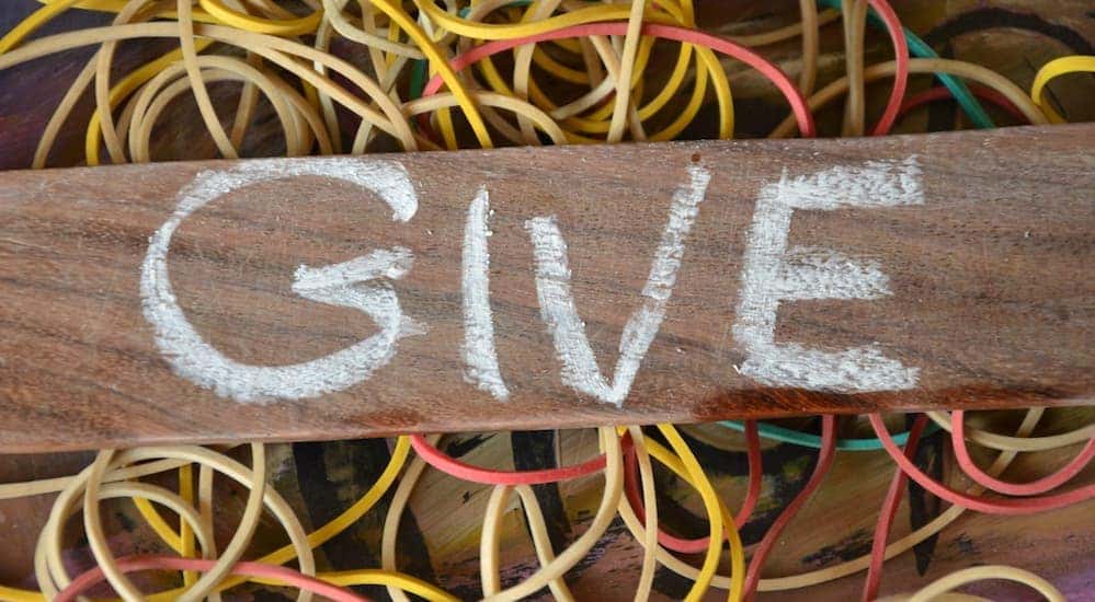 The word 'Give' written on a piece of wood that is sitting on a pile of rubber bands