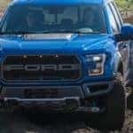 A 2017 blue Ford Raptor, which is a popular choice among consumers who Buy Used Cars in Columbus, OH, is driving through a mud pit.