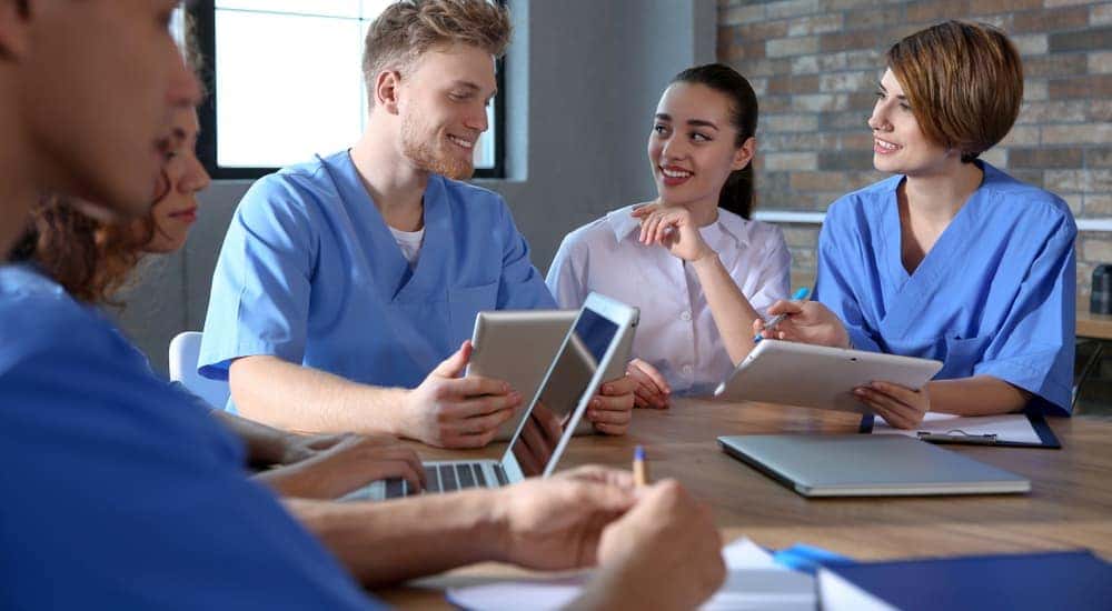 Nursing students in scrubs sitting at a table on their tablets and laptops