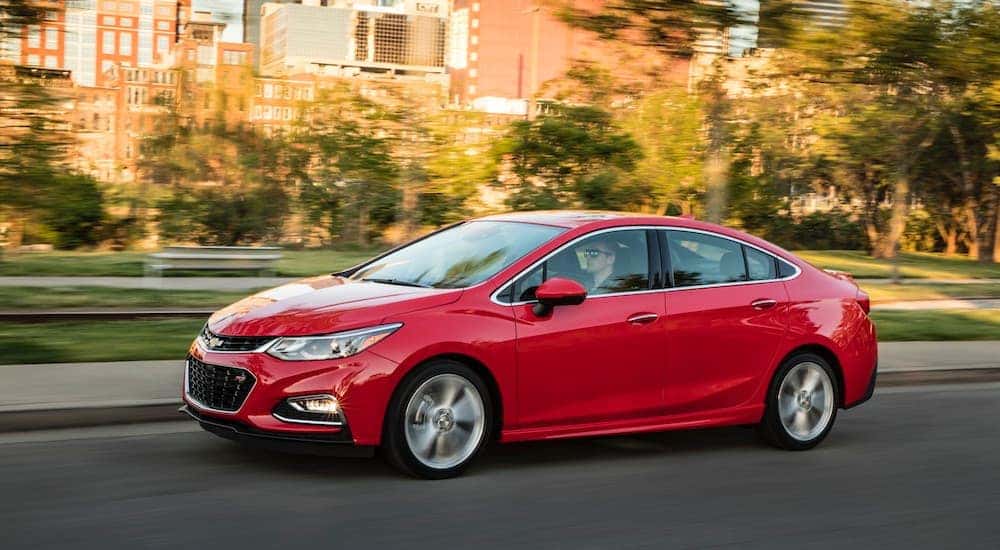 A red 2016 Chevy Cruze is driving past a city park.