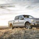 A silver 2018 Ford F-150 is parked in a grassy field at dusk.