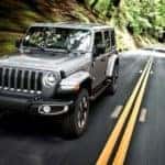 A silver 2019 Jeep Wrangler, popular among used Jeeps for sale, is driving on a tree-lined road.