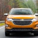 An orange 2018 Chevy Equinox is driving forward on a tree lined highway.