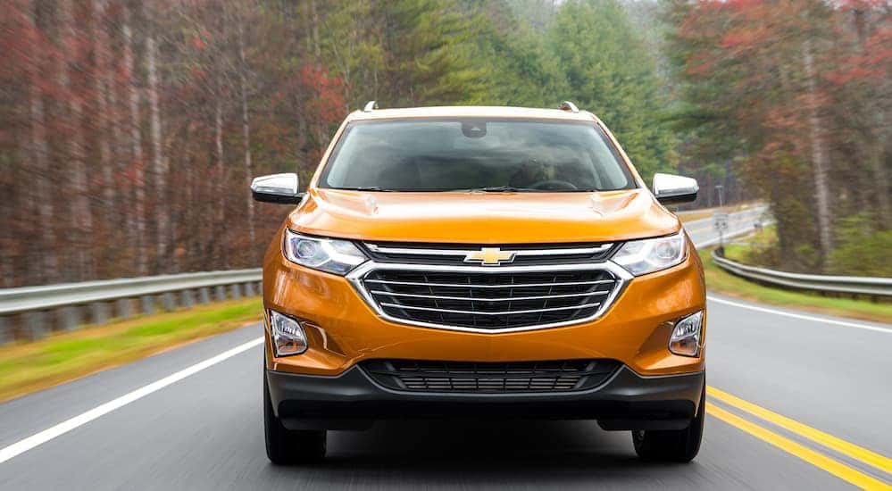 Egy narancssárga 2018-as Chevy Equinox halad előre egy fákkal szegélyezett autópályán.