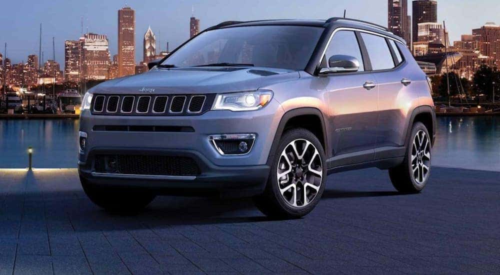 A grey 2020 Jeep Compass is parked on a dock with a city skyline lit up behind it. 