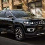 A black 2018 Jeep Compass is driving past buildings near Indianapolis, IN.