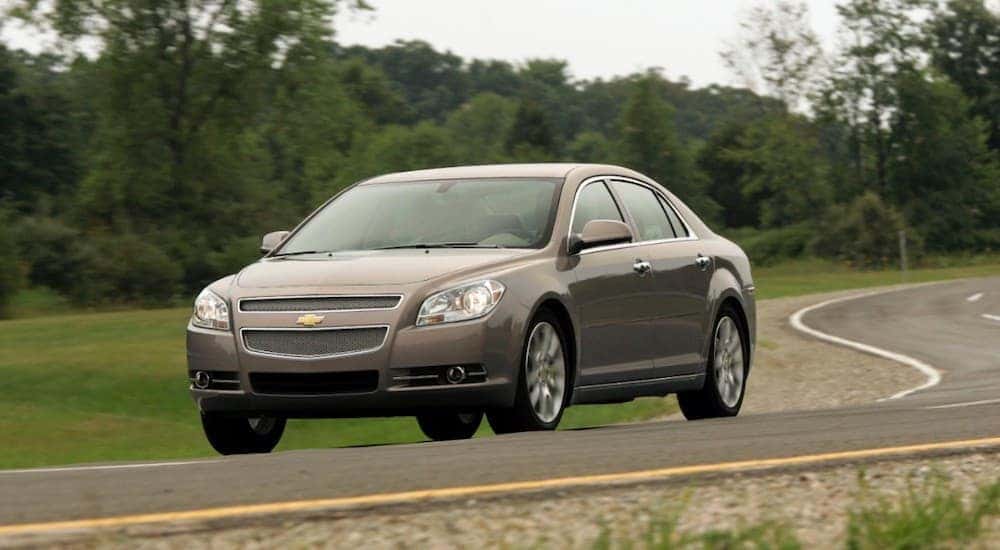 A grey 2012 Chevy Malibu, which is a popular buy for used cars in Indianapolis, is driving on a winding road.