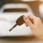 A key for a used car is held up in front of an out-of-focus white car.