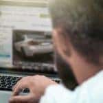 A view is shown over the shoulder of a man who is shopping for cars in Indianapolis on a laptop.