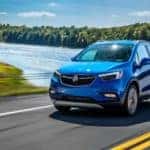 A blue 2019 Buick Encore is driving past a lake.