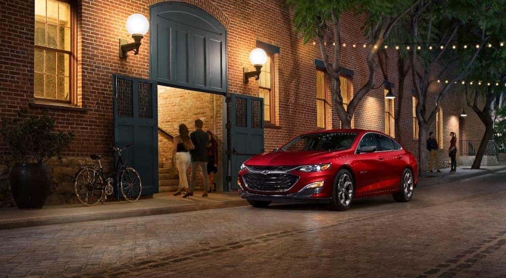 One of the popular used cars in Indianapolis, a red 2019 Chevy Malibu is parked outside a brick building at night.