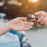 An online car dealership delivery driver is handing customer car keys in front of a blue sedan in Kentucky.