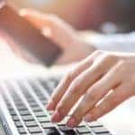 A closeup shows a woman's hands using a laptop to shop for a car online.