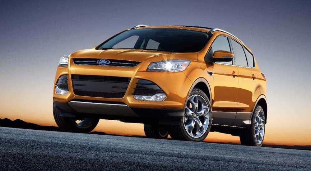 A gold 2013 Ford Escape is shown against a blue and yellow sunset sky,