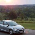 A silver 2018 Chevy Cruze sedan from an online car dealership is parked with a setting sun in the background.
