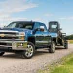 A blue 2018 Chevy Silverado 2500HD is towing construction equipment on a gravel road.