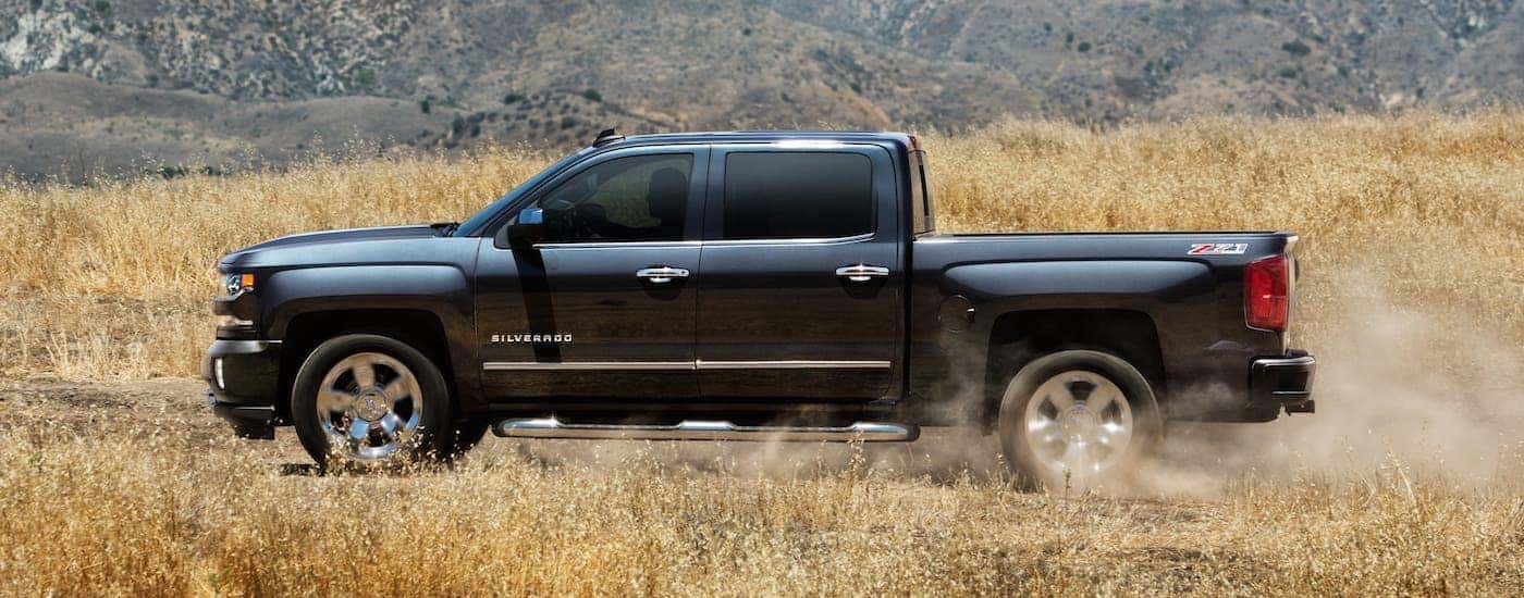 A black 2018 Chevy Silverado 1500 is shown from the side driving on a dirt road after leaving an Indianapolis used truck dealer.