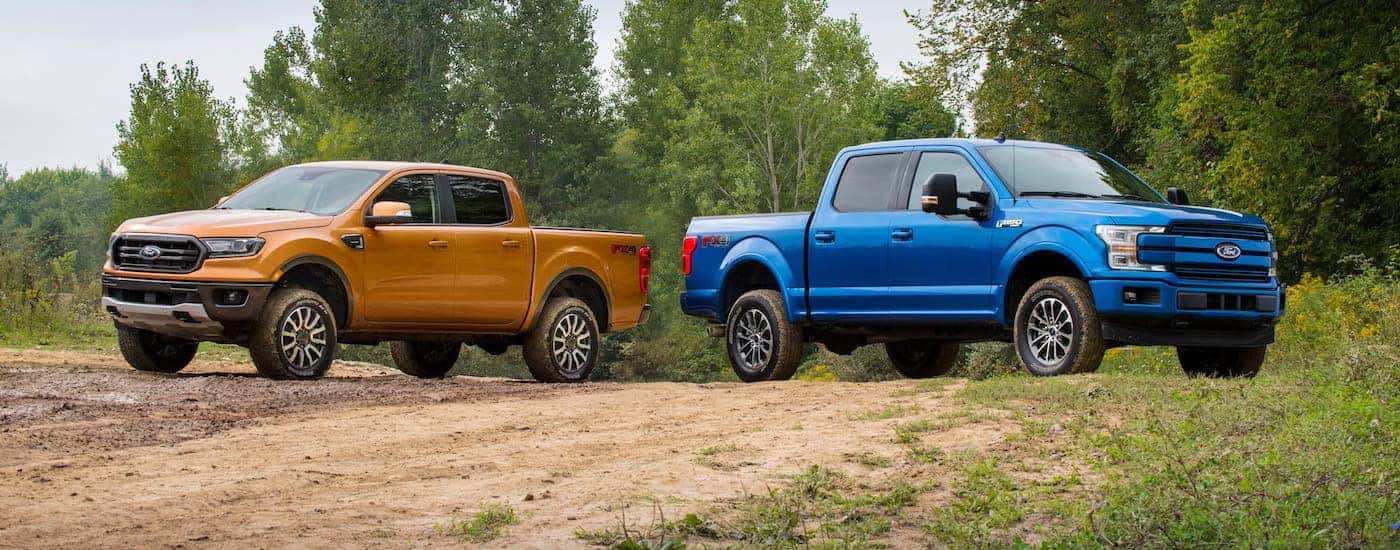 An orange 2019 Ford Ranger and a blue 2019 Ford F-150 are parked on a dirt road facing away from each other.