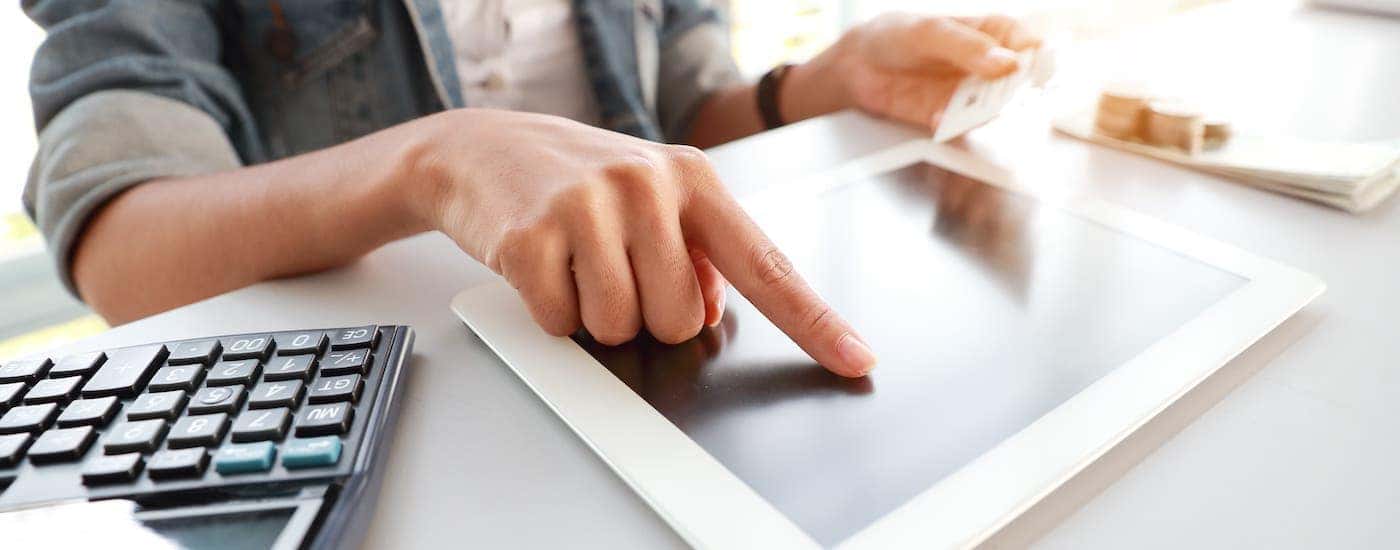 A closeup shows hands entering credit card information on a tablet next to a calculator.