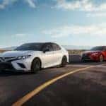 A white and a red 2019 Toyota Camry, often found at online car dealers, are driving on a racetrack.