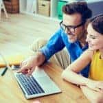 A smiling couple are looking at a laptop from their home while looking at online car sales sites.