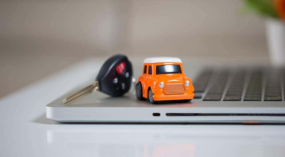An orange toy car and a car key are sitting on a laptop.