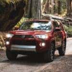 A dark red 2020 Toyota 4Runner is driving through the woods.