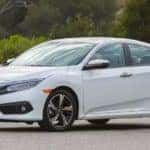 A white 2016 Honda Civic is parked in front of trees.