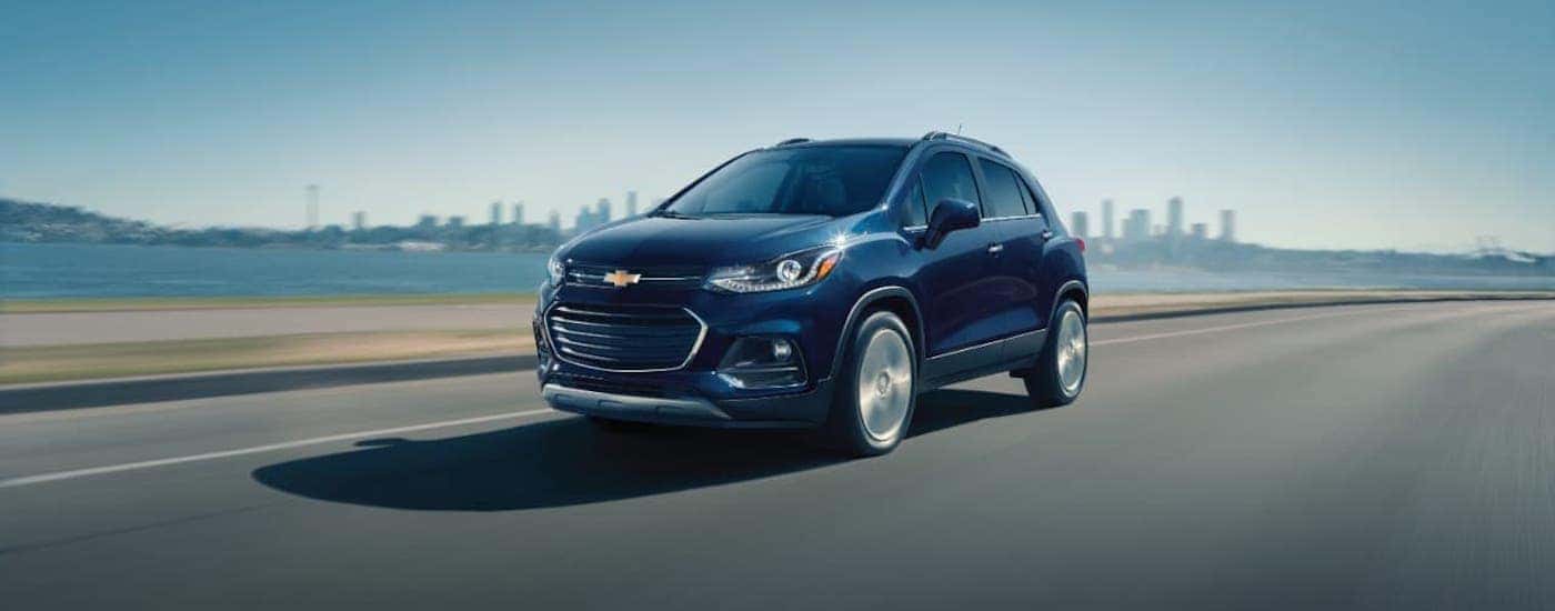 A dark blue 2018 Chevy Trax is driving away from a city.