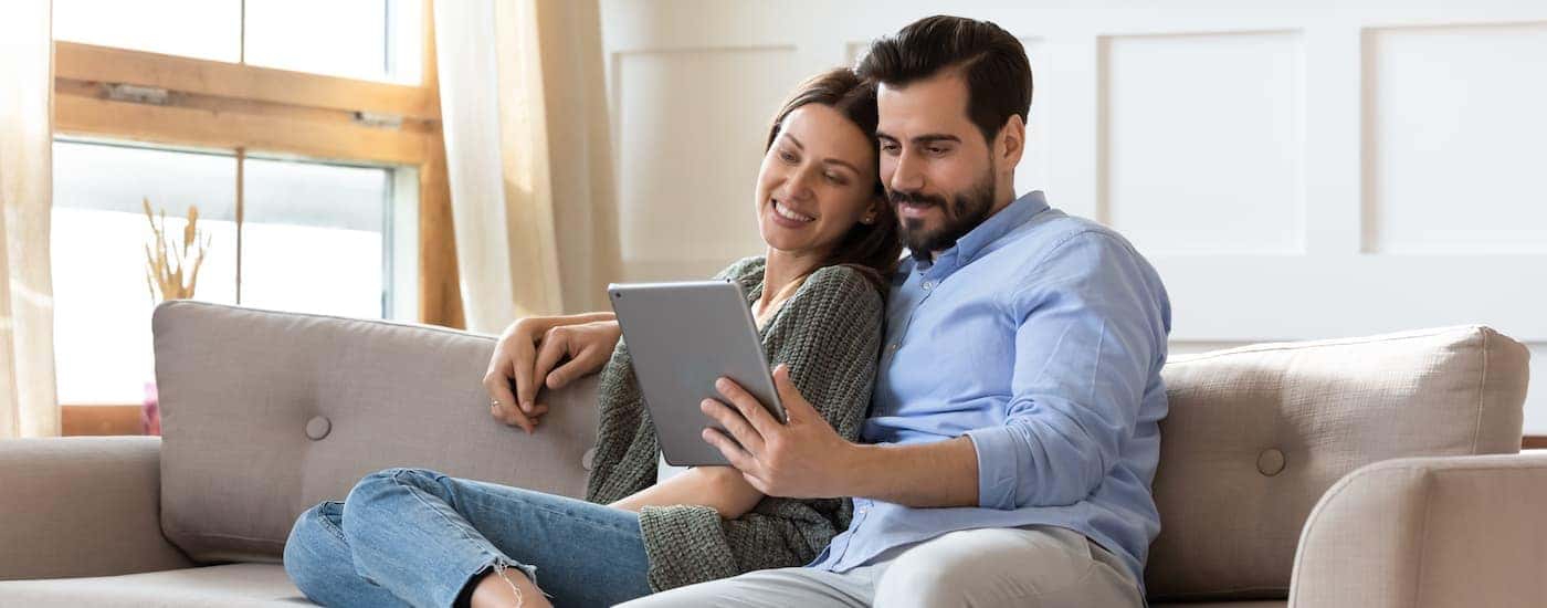 A couple is online car shopping from a tablet while on a couch.