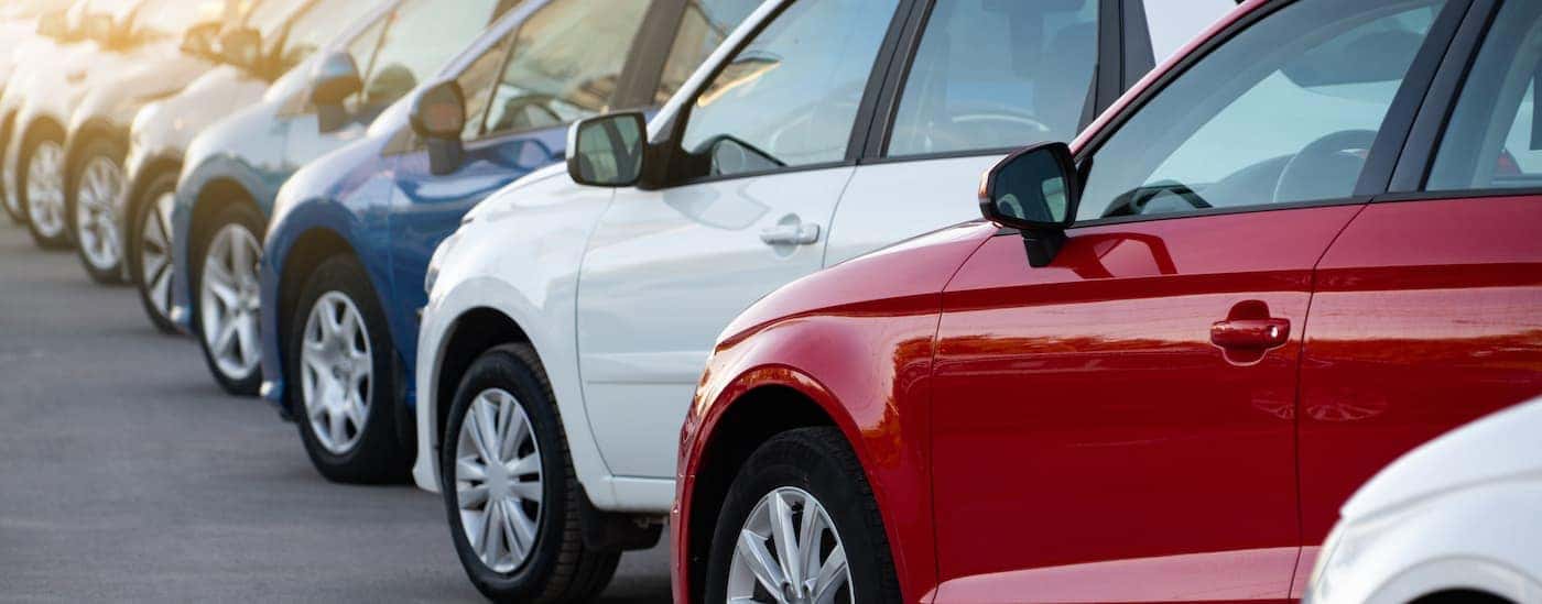 Blue, white, and red sedans are shown in a row in a parking lot.