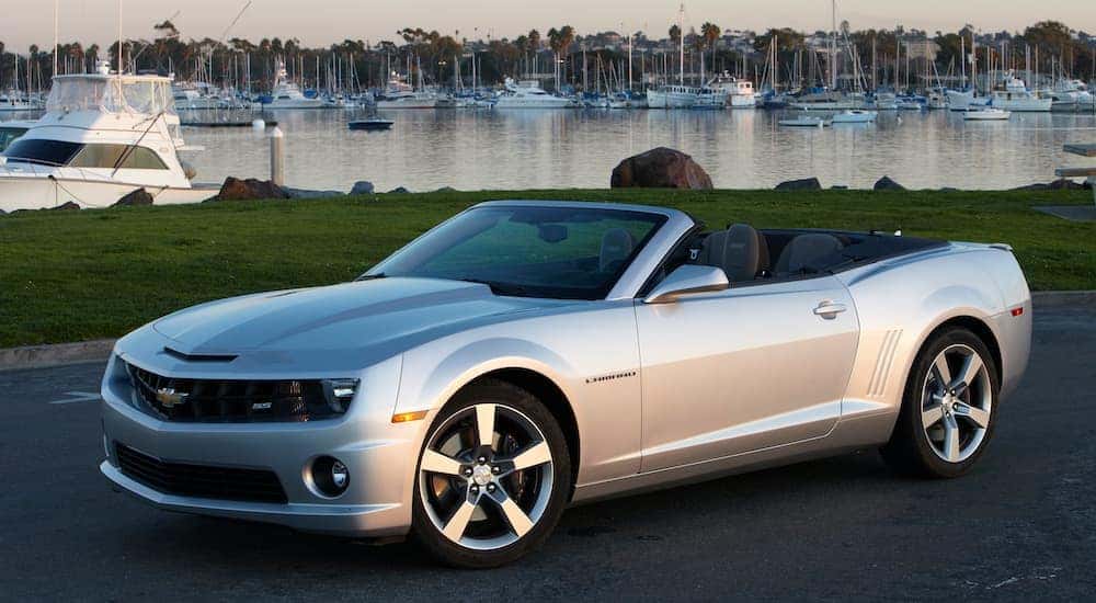Side angled view of a silver 2012 Chevy Camaro SS convertible parked in front of a bay full of boats