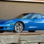 A blue 2013 C6 Chevy Corvette Grand Sport is shown from the side parked in from of a brick garage.