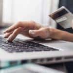 A woman is entering her credit card information into her laptop while looking at Online car sales in Indianapolis.