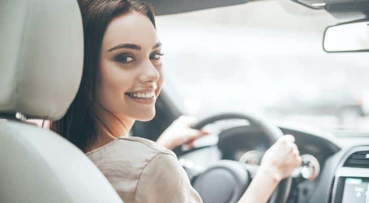 A smiling woman is shown driving a car.
